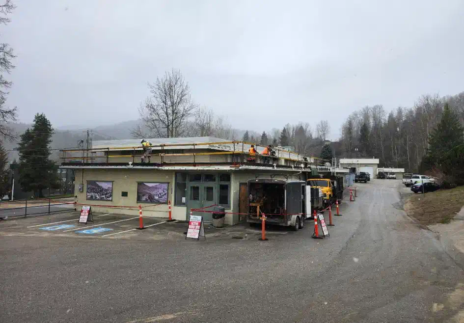 Crew working a commercial flat roof behind perimeter guardrails, work site coned off below — West Kootenays