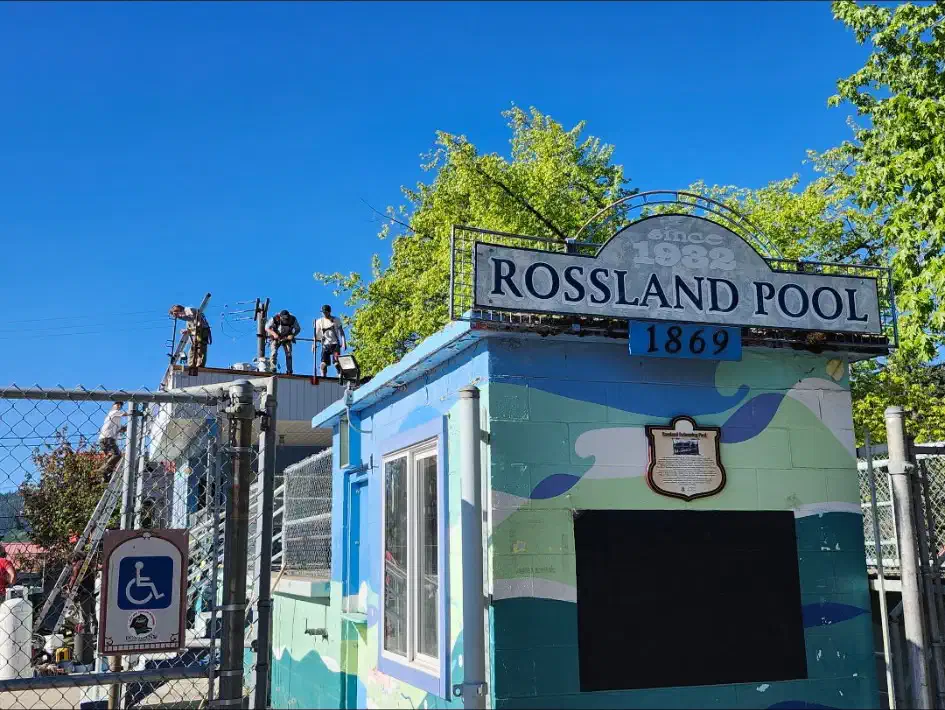 Roofing crew at work on the flat roof of a heritage community pool building — Rossland