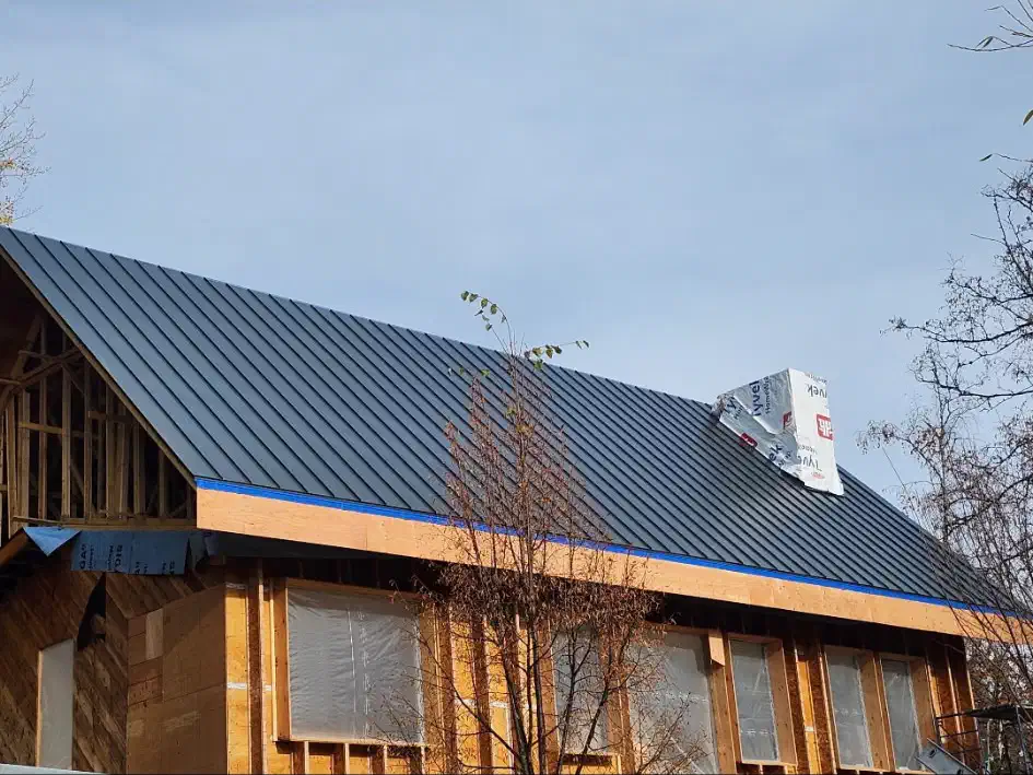 New dark metal panel roof installed on a timber-framed house under construction — West Kootenays