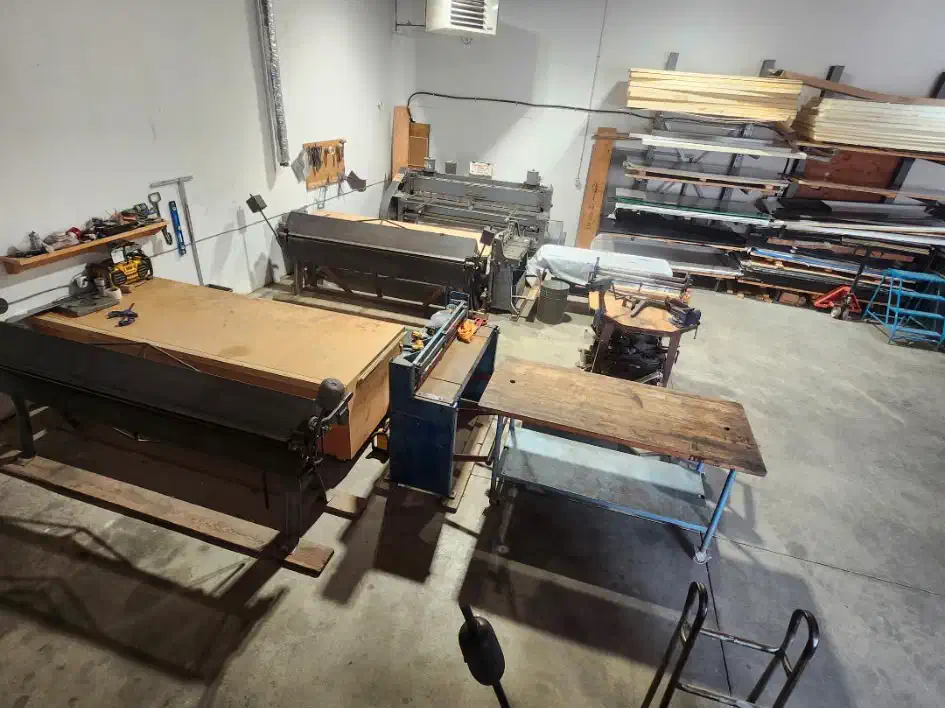 Sheet-metal fabrication shop with brakes, a shear, workbenches and racks of flashing stock — West Kootenays