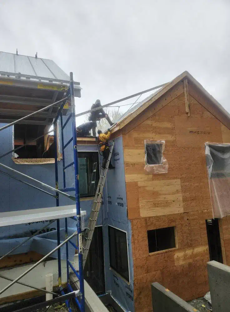 Crew installing standing seam steel roofing panels on a new home — West Kootenays