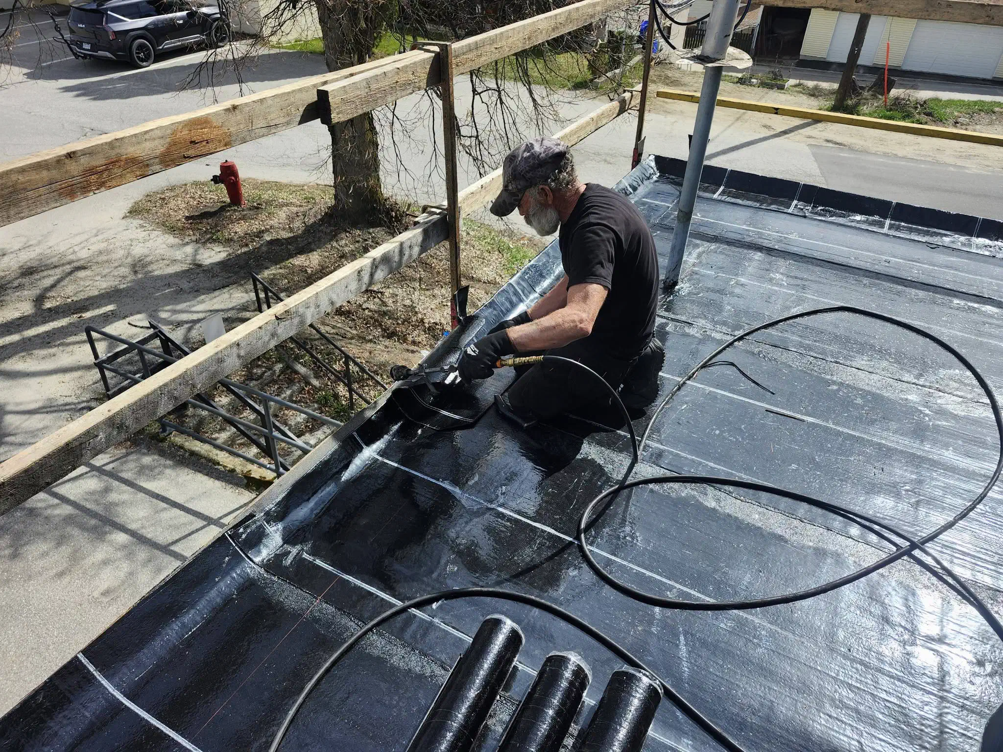 Roofer sealing torch-on membrane seams at the roof edge of a flat roof — West Kootenays